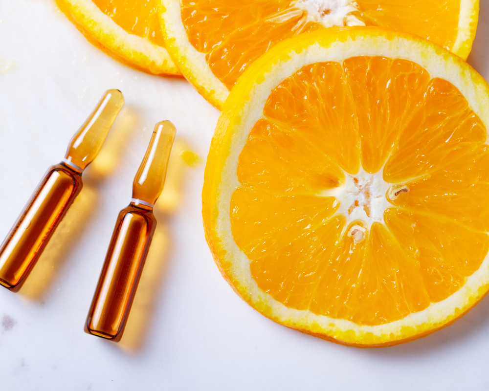Fonte: Canva pedaços de uma laranja com duas ampolas de Vitamina C líquida