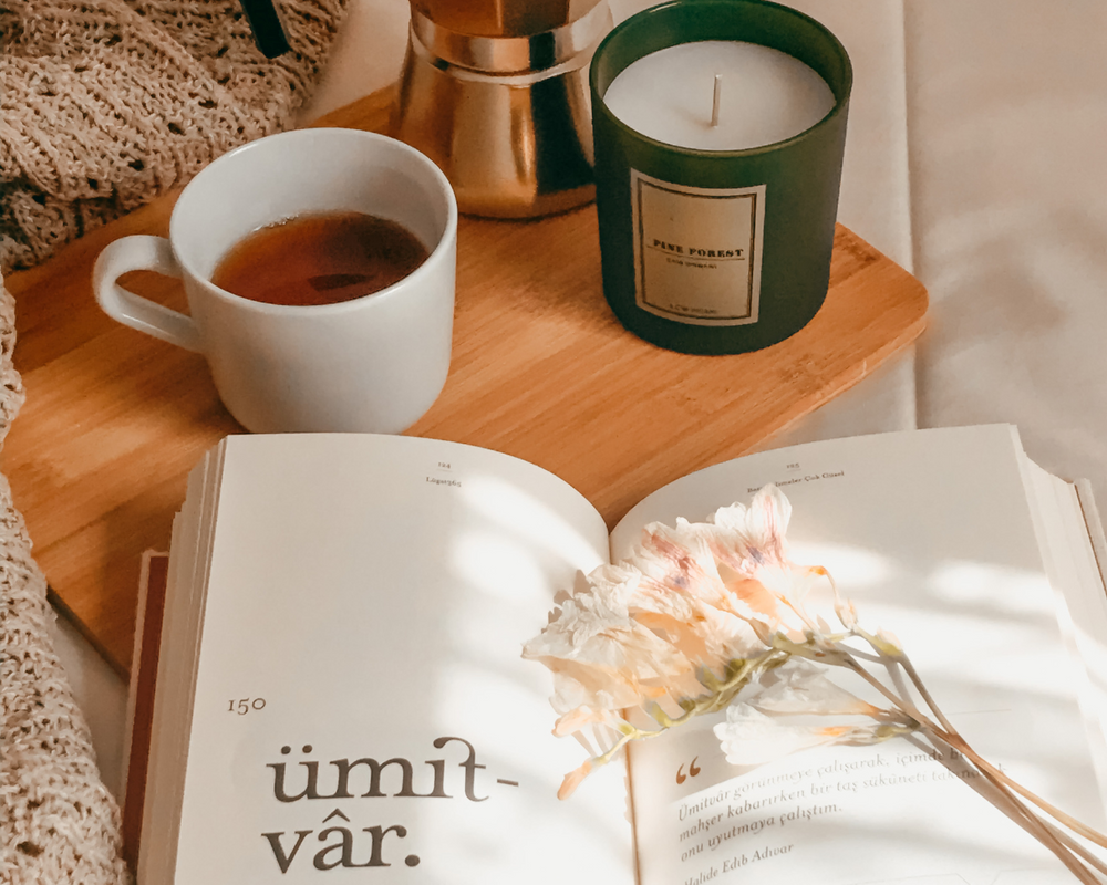 Fonte: Canva um livro aberto com uma flor dentro e ao lado uma caneca de café e uma vela aromática