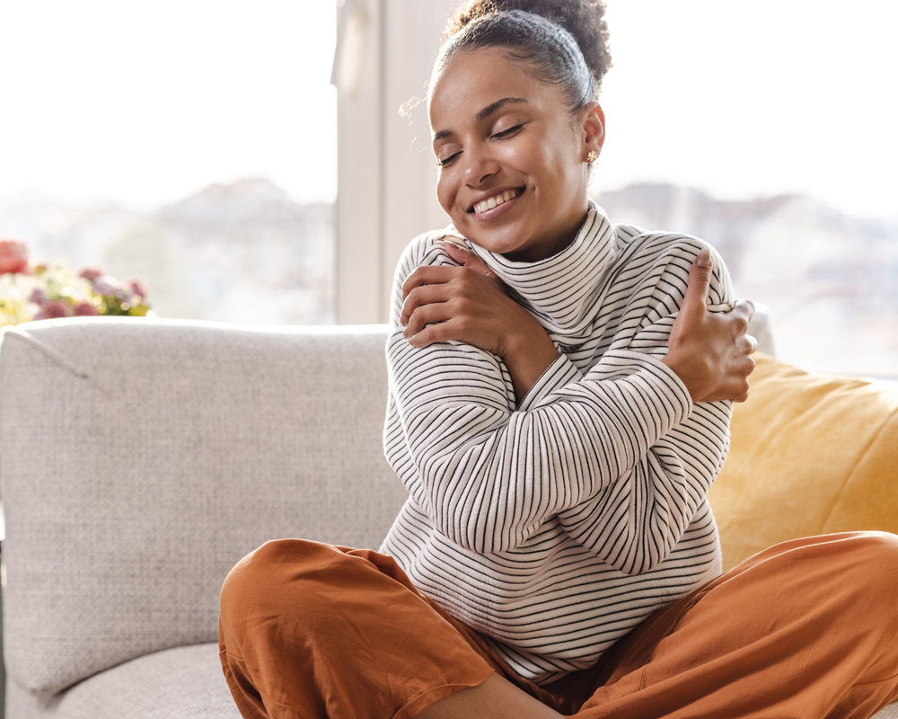 Uma mulher negra sentada em um sofá se abraçando