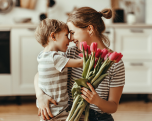 mãe carregando o filho com um buque de flores na outra mão